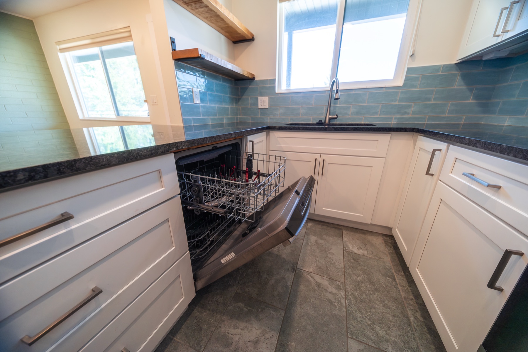 Kitchen detail with blue tile backsplash, dishwasher, and window