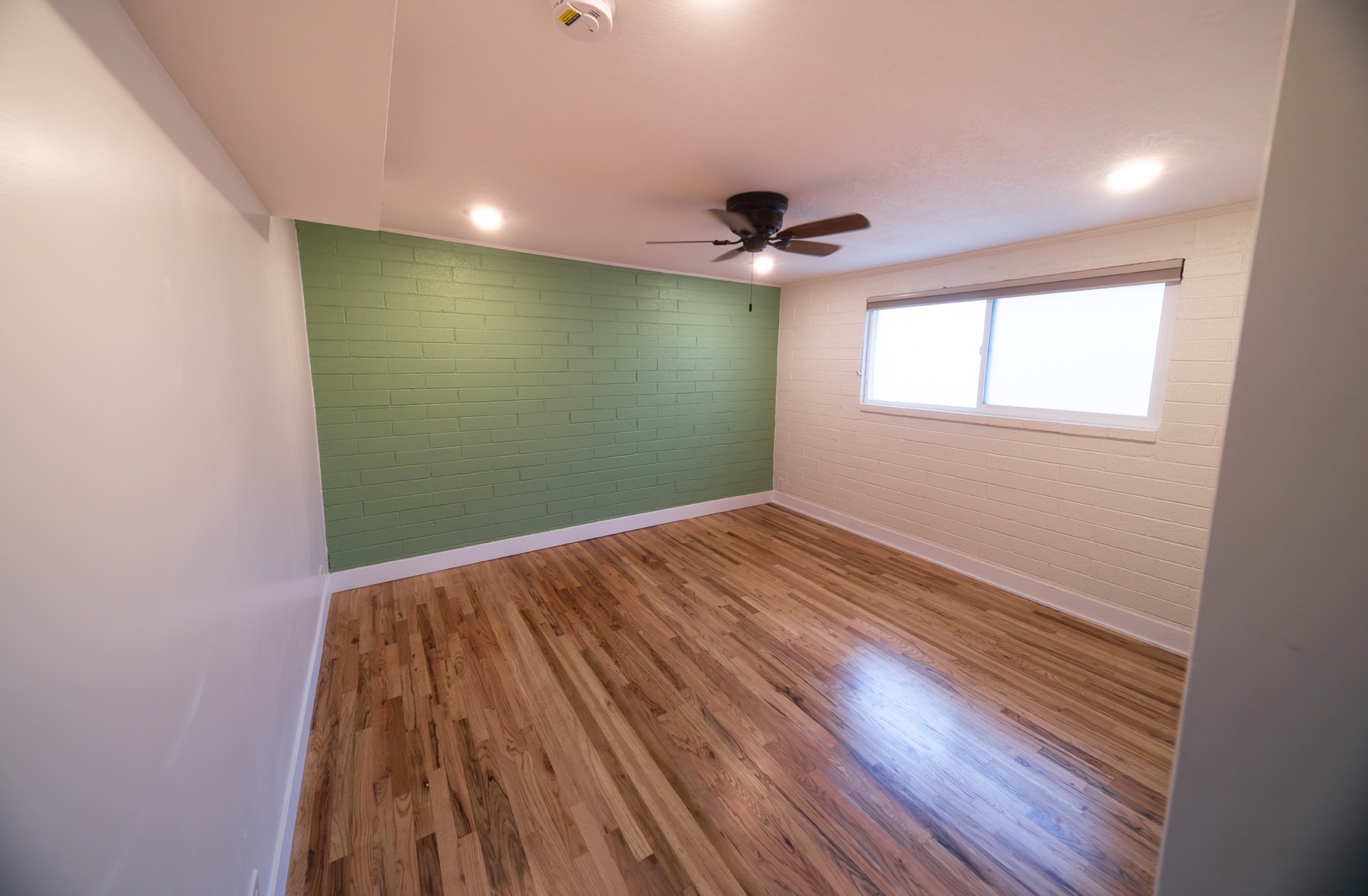Bedroom with a green accent wall, ceiling fan, and hardwood floors