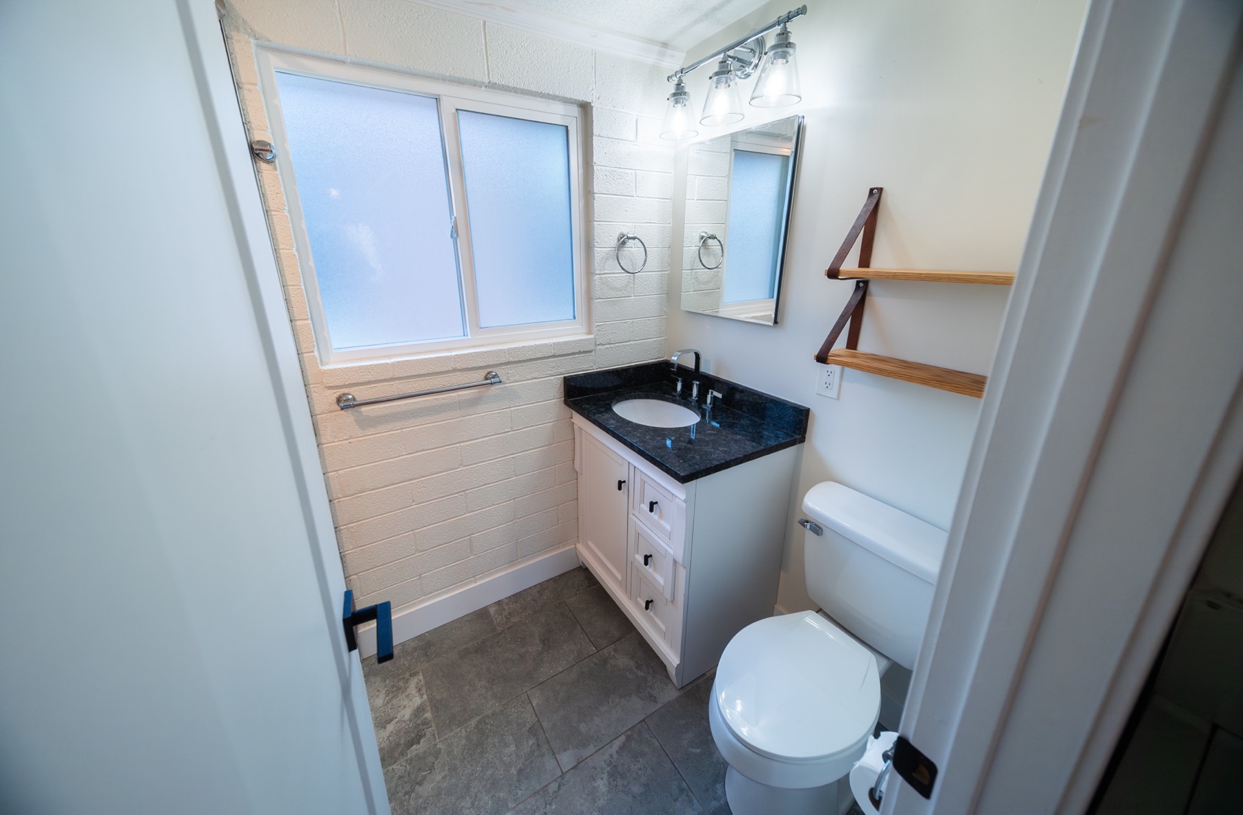 Renovated bathroom with vanity, dark counter, and open shelving