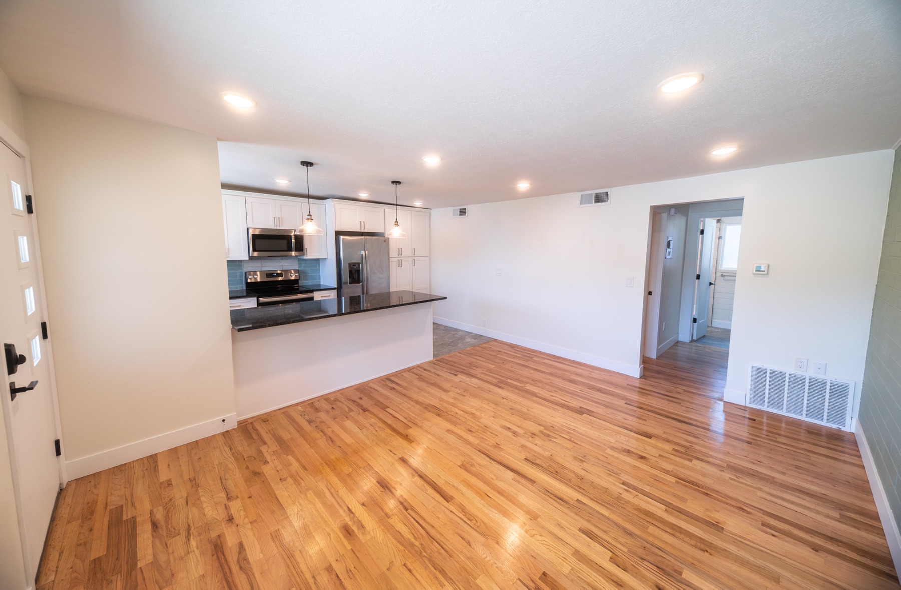 Open-plan living area looking toward the kitchen and hallway, with hardwood floors