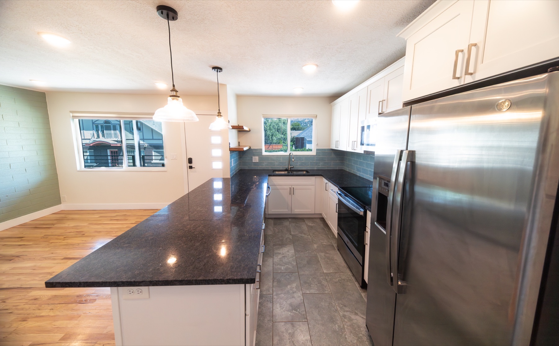 Kitchen and dining area with island, dark counters, green accent wall, and windows