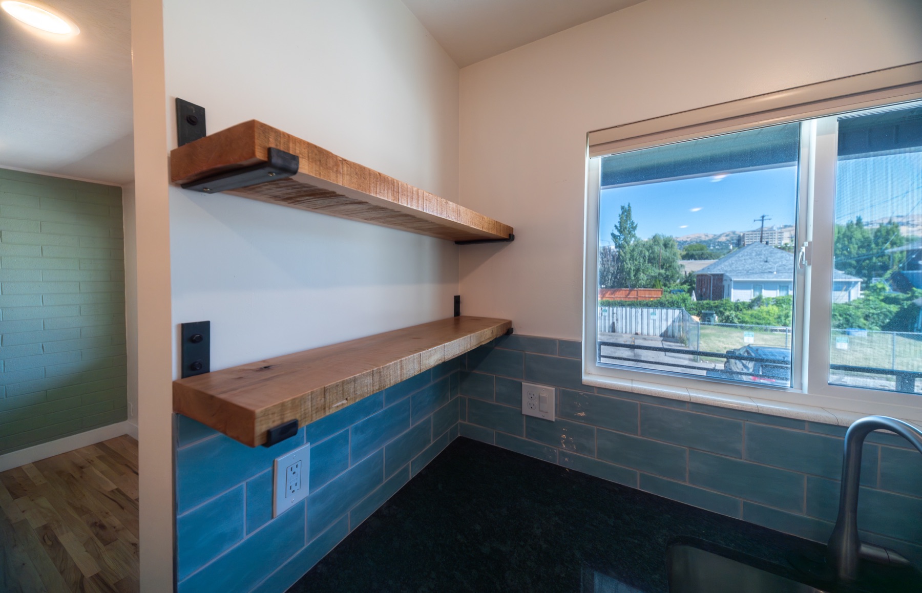 Floating wood shelves above a blue-tile counter beside a bright window